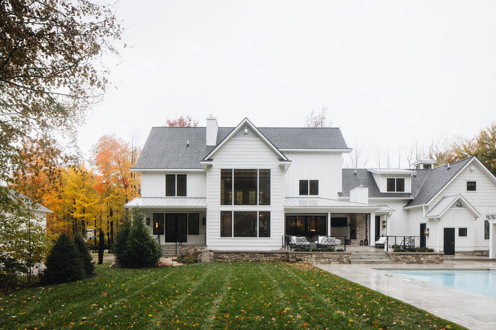 Exterior - Modern farmhouse exterior near Grand Rapids, Michigan featuring a stone patio, in-ground swimming pool, pool deck, board and batten siding, black windows, gray shingle roof, and black doors.