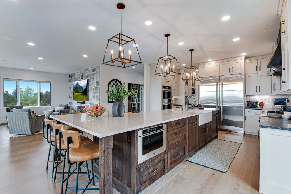 Inspiration for a large country u-shaped open plan kitchen in Denver with a farmhouse sink, recessed-panel cabinets, beige cabinets, quartz benchtops, beige splashback, stone tile splashback, stainless steel appliances, medium hardwood floors, with island, brown floor, white benchtop and wood.