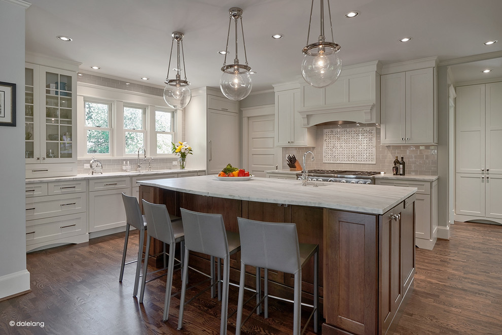 Design ideas for a large arts and crafts l-shaped eat-in kitchen in Seattle with an undermount sink, shaker cabinets, white cabinets, beige splashback, ceramic splashback, stainless steel appliances, dark hardwood floors, with island, marble benchtops, brown floor and white benchtop.