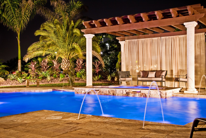 Inspiration for a large tropical backyard custom-shaped pool in Miami with a hot tub and natural stone pavers.