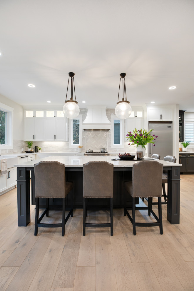 Example of a huge minimalist u-shaped light wood floor and brown floor eat-in kitchen design in Portland with a farmhouse sink, shaker cabinets, white cabinets, quartz countertops, white backsplash, ceramic backsplash, stainless steel appliances, an island and white countertops