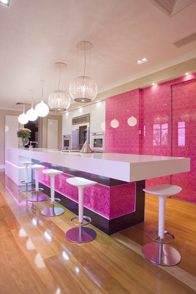 Photo of a large contemporary galley kitchen in Los Angeles with flat-panel cabinets, quartz benchtops, pink splashback, glass sheet splashback, stainless steel appliances, light hardwood floors and with island.