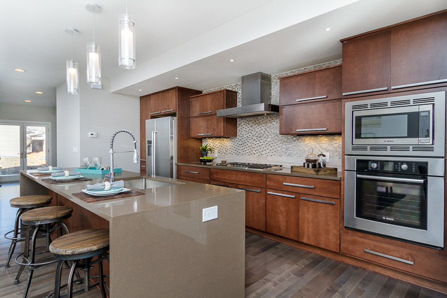 This is an example of a large modern galley open plan kitchen in Denver with an undermount sink, flat-panel cabinets, medium wood cabinets, solid surface benchtops, beige splashback, stainless steel appliances, dark hardwood floors, with island and brown floor.