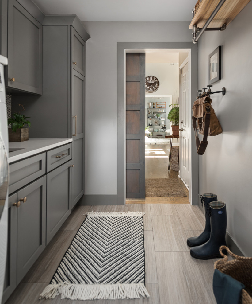 Photo of a mid-sized transitional single-wall utility room in Chicago with an undermount sink, shaker cabinets, grey cabinets, quartz benchtops, multi-coloured splashback, cement tile splashback, grey walls, porcelain floors, a side-by-side washer and dryer, grey floor and white benchtop.