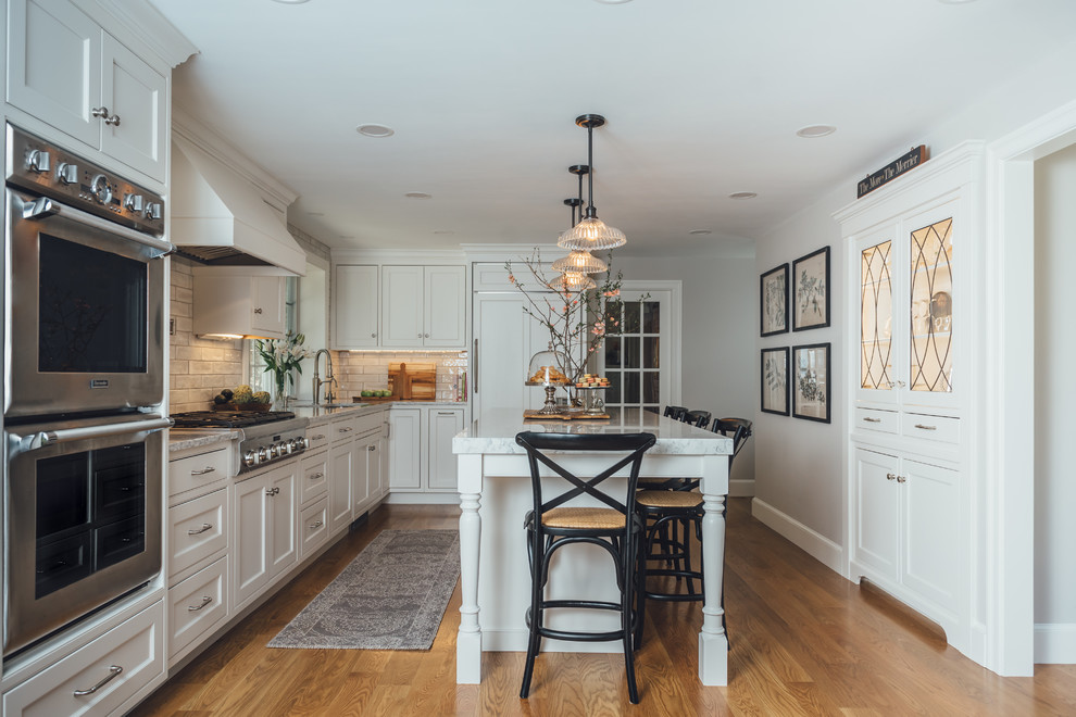 This is an example of a traditional l-shaped kitchen in Boston with white cabinets, quartz benchtops, panelled appliances, beaded inset cabinets, white splashback, subway tile splashback, medium hardwood floors, with island, brown floor and grey benchtop.