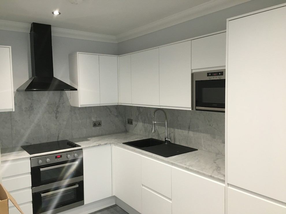Photo of a medium sized modern u-shaped open plan kitchen in London with a built-in sink, flat-panel cabinets, white cabinets, marble worktops, grey splashback, black appliances, plywood flooring and an island.