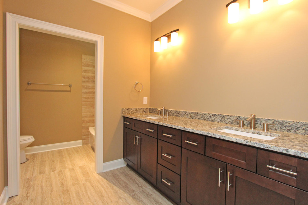 This is an example of a mid-sized traditional master bathroom in Atlanta with recessed-panel cabinets, dark wood cabinets, an alcove tub, a shower/bathtub combo, a two-piece toilet, beige tile, porcelain tile, yellow walls, porcelain floors, an undermount sink, granite benchtops, beige floor, a shower curtain and multi-coloured benchtops.