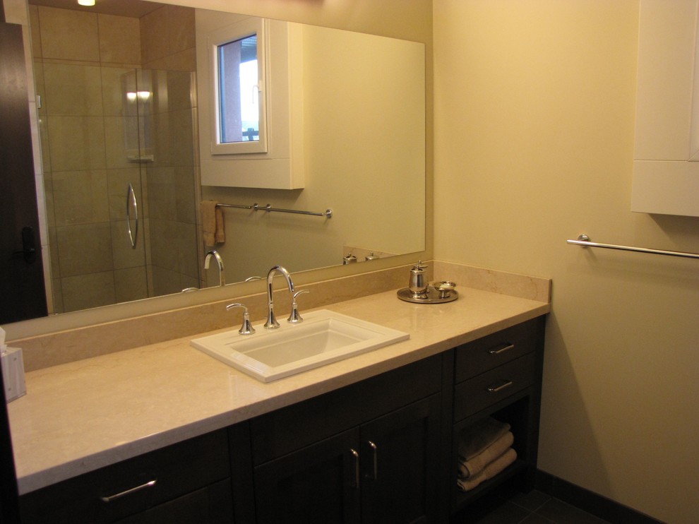 This is an example of a mid-sized mediterranean master bathroom in Vancouver with shaker cabinets, dark wood cabinets, an alcove shower, beige tile, ceramic tile, beige walls, a drop-in sink, limestone benchtops and a hinged shower door.