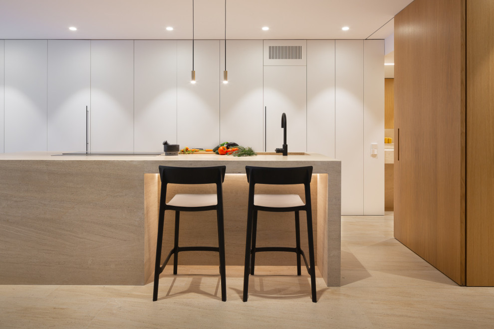 This is an example of an expansive contemporary l-shaped open plan kitchen in Alicante-Costa Blanca with flat-panel cabinets, white cabinets, limestone benchtops, with island, brown benchtop, an integrated sink, panelled appliances and beige floor.