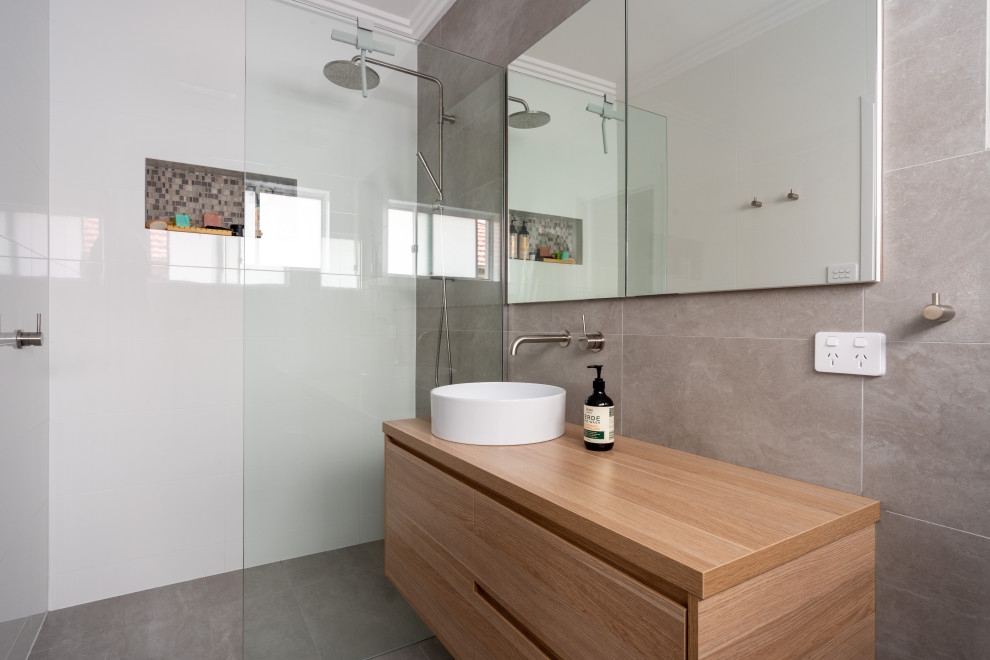 This is an example of a mid-sized contemporary 3/4 bathroom in Wollongong with furniture-like cabinets, light wood cabinets, an open shower, white tile, ceramic tile, white walls, light hardwood floors, a console sink, multi-coloured floor, a niche, a single vanity and a floating vanity.