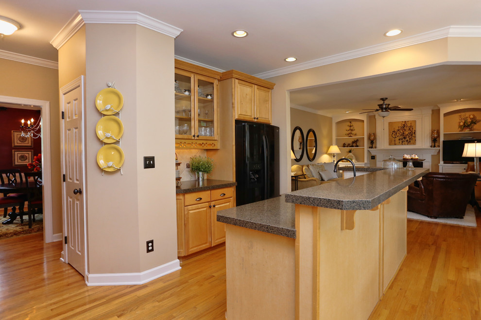 Example of a mid-sized transitional u-shaped medium tone wood floor and brown floor open concept kitchen design in Raleigh with a double-bowl sink, raised-panel cabinets, medium tone wood cabinets, quartz countertops, beige backsplash, limestone backsplash, black appliances, an island and brown countertops