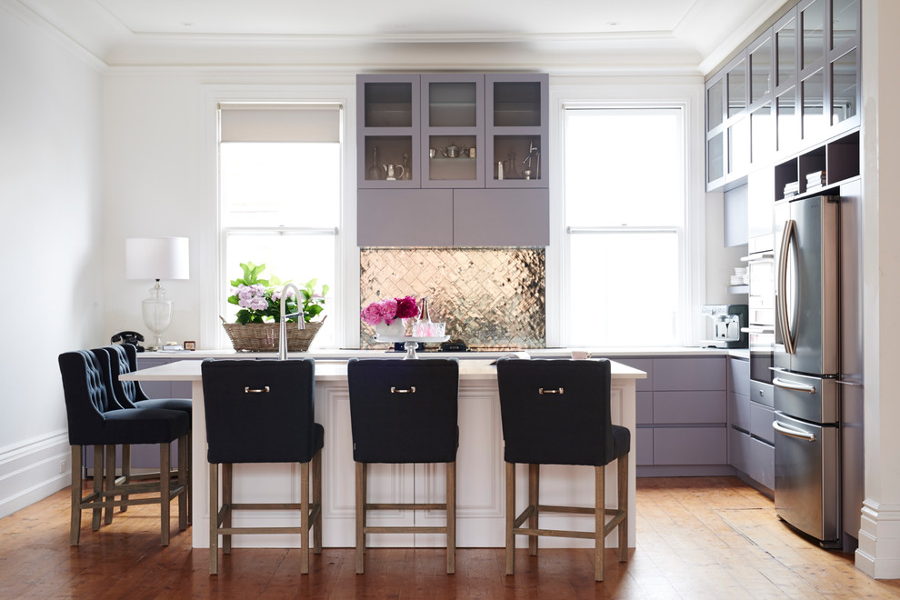 This is an example of a transitional l-shaped kitchen in Sydney with glass-front cabinets, purple cabinets, metallic splashback, metal splashback, stainless steel appliances, medium hardwood floors, with island and white benchtop.