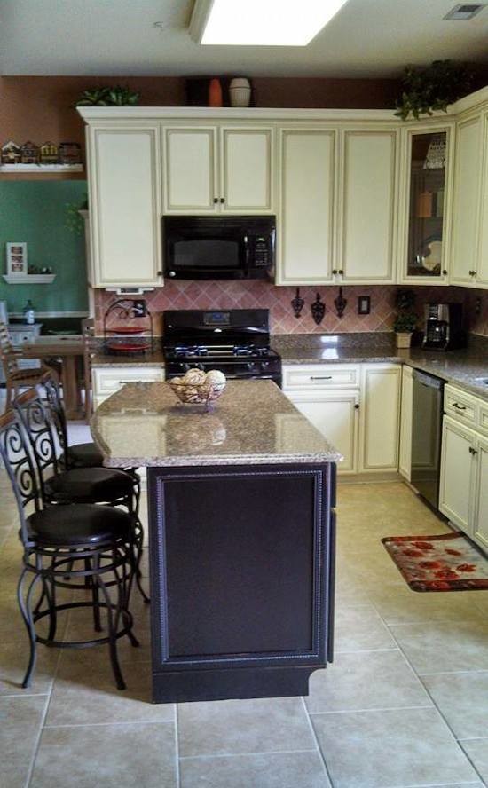 На фото: угловая кухня среднего размера с обеденным столом, белыми фасадами, гранитной столешницей, розовым фартуком, фартуком из керамической плитки, черной техникой, полом из известняка и островом с