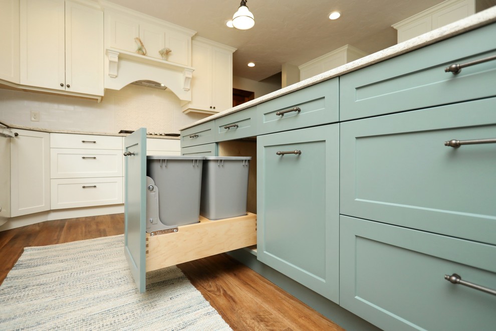 Example of a transitional vinyl floor and brown floor kitchen design with an undermount sink, white cabinets, quartz countertops, white backsplash, subway tile backsplash, stainless steel appliances, an island and beige countertops
