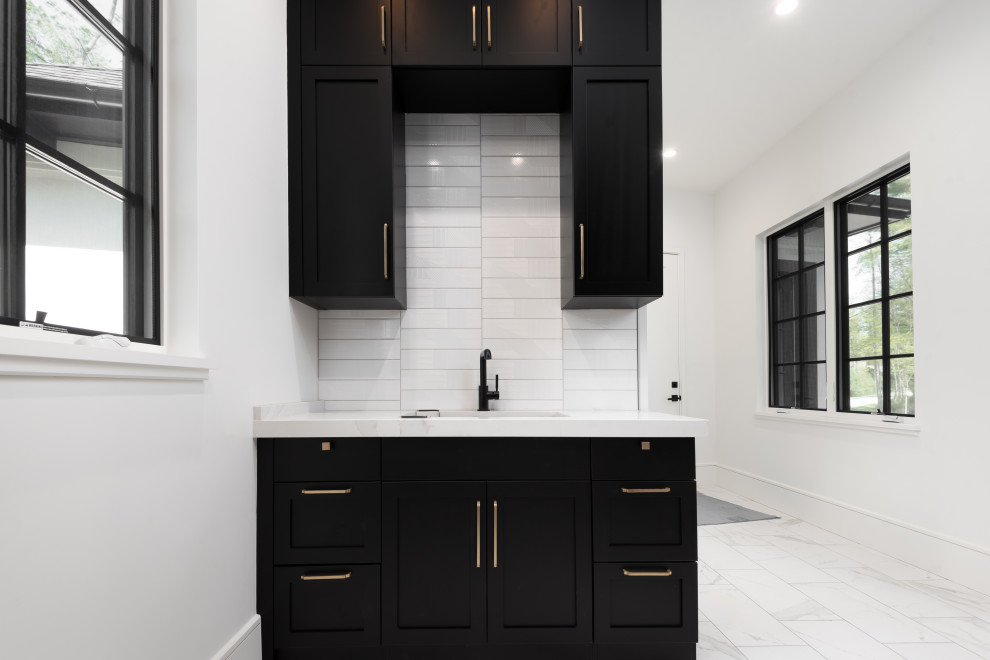 Mid-sized transitional ceramic tile and white floor utility room photo with an undermount sink, black cabinets, quartz countertops, white backsplash, subway tile backsplash, white walls, a side-by-side washer/dryer and white countertops