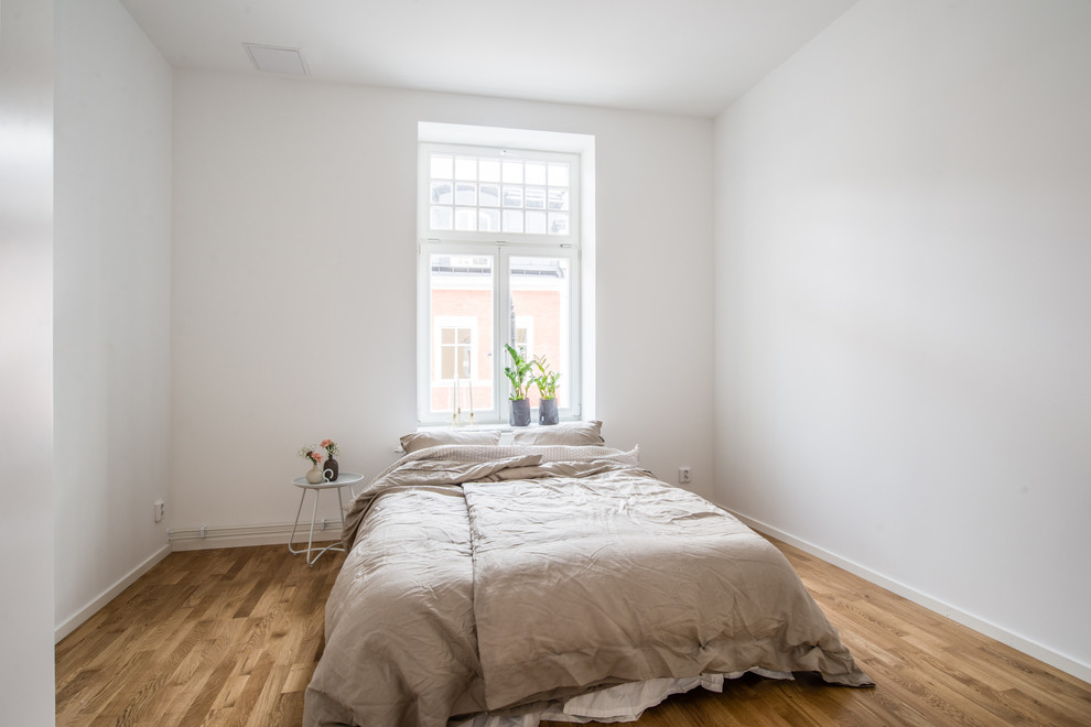 Design ideas for a scandinavian bedroom in Stockholm with white walls, medium hardwood floors and brown floor.
