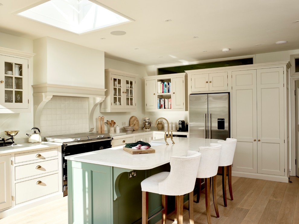 Inspiration for a mid-sized traditional l-shaped kitchen in London with a farmhouse sink, quartzite benchtops, white splashback, stainless steel appliances, with island, beaded inset cabinets, beige cabinets, medium hardwood floors, brown floor and white benchtop.