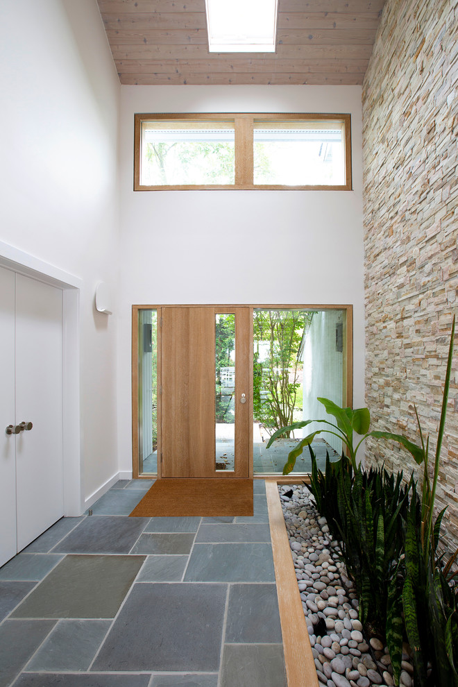 This is an example of a large contemporary entry hall in New York with white walls, a single front door, a medium wood front door and grey floor.