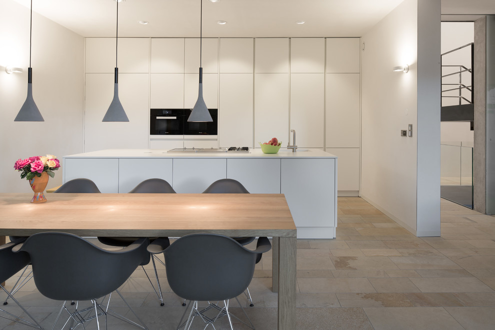 Large contemporary single-wall eat-in kitchen in Munich with flat-panel cabinets, white cabinets, white splashback, black appliances, with island, travertine floors, an integrated sink, beige floor and white benchtop.