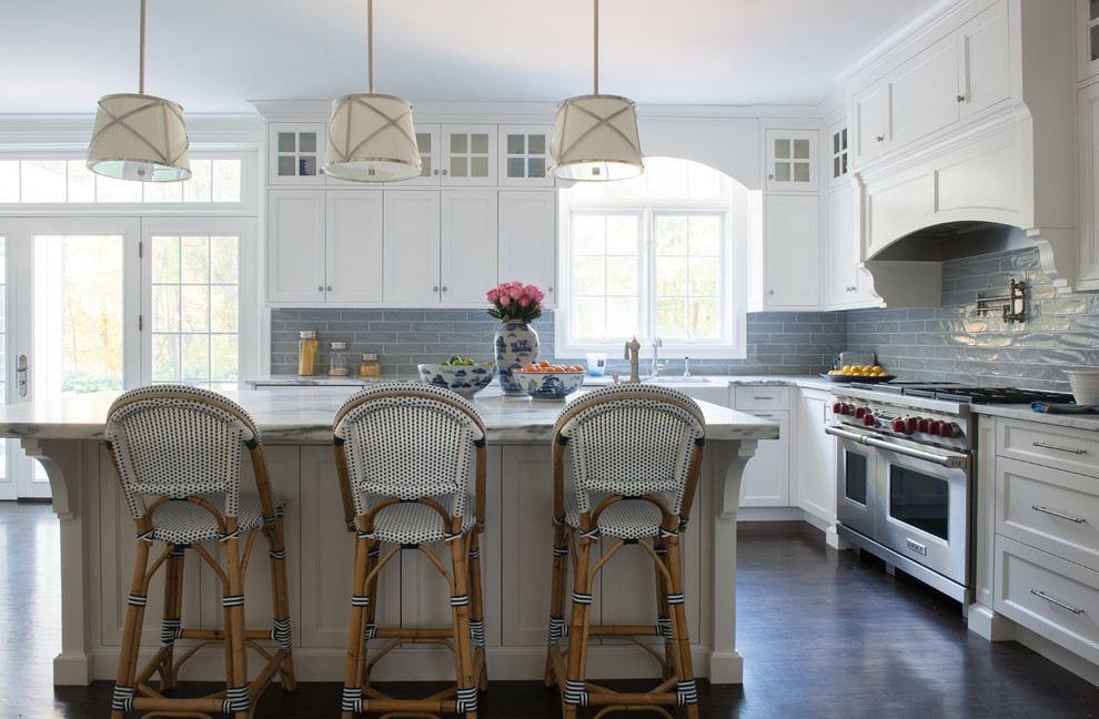 This is an example of a mid-sized transitional u-shaped open plan kitchen in New York with a farmhouse sink, shaker cabinets, white cabinets, marble benchtops, grey splashback, subway tile splashback, stainless steel appliances, dark hardwood floors, with island, brown floor and grey benchtop.