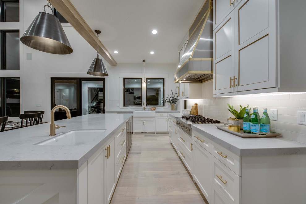 Country u-shaped eat-in kitchen in Other with a farmhouse sink, shaker cabinets, white cabinets, white splashback, subway tile splashback, stainless steel appliances, light hardwood floors, with island, beige floor and grey benchtop.