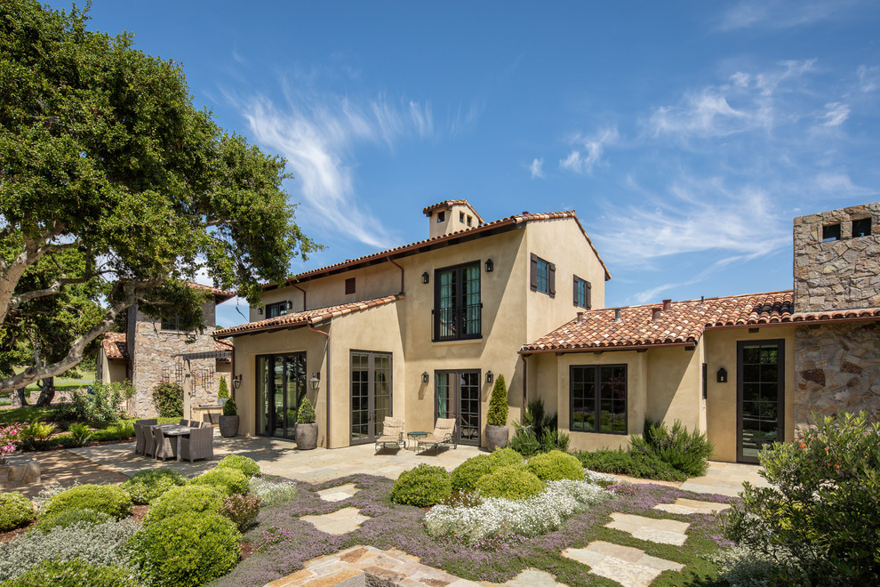 This is an example of a large mediterranean two-storey stucco beige house exterior in Orange County with a gable roof and a tile roof.