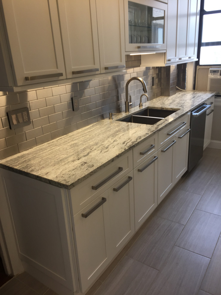 This is an example of a transitional eat-in kitchen in New York with white cabinets, metallic splashback, metal splashback, stainless steel appliances and shaker cabinets.