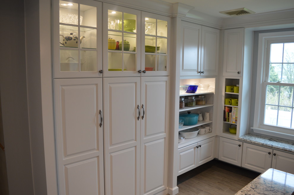 Large transitional u-shaped ceramic tile and gray floor home design photo with a farmhouse sink, raised-panel cabinets, white cabinets, quartz countertops, gray backsplash, glass tile backsplash, stainless steel appliances and an island