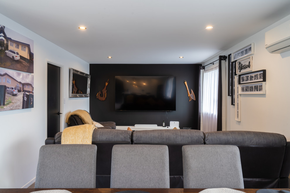 Imagen de cine en casa abierto actual de tamaño medio con paredes negras, suelo laminado, televisor colgado en la pared y suelo gris