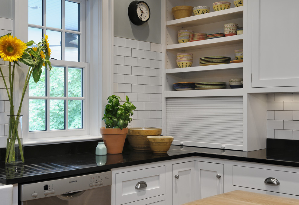This is an example of a traditional eat-in kitchen in New York with a farmhouse sink, recessed-panel cabinets, white cabinets, soapstone benchtops, white splashback, subway tile splashback and stainless steel appliances.