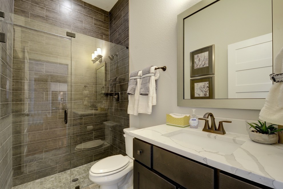This is an example of a transitional 3/4 bathroom in Jacksonville with shaker cabinets, brown cabinets, an alcove shower, a two-piece toilet, brown tile, grey walls, an undermount sink, a hinged shower door and white benchtops.