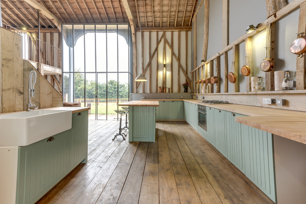 This is an example of an expansive country galley open plan kitchen in Other with a farmhouse sink, green cabinets, light hardwood floors and with island.