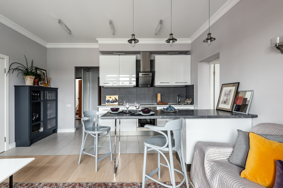 This is an example of a scandinavian single-wall open plan kitchen in Moscow with flat-panel cabinets, white cabinets, grey splashback, stainless steel appliances, with island and grey benchtop.
