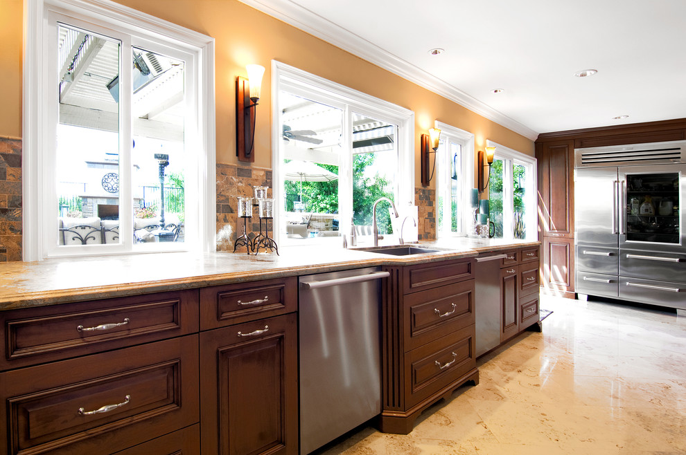 Photo of an expansive transitional galley eat-in kitchen in Orange County with a single-bowl sink, recessed-panel cabinets, medium wood cabinets, limestone benchtops, beige splashback, limestone splashback, stainless steel appliances, porcelain floors, multiple islands, beige floor and beige benchtop.