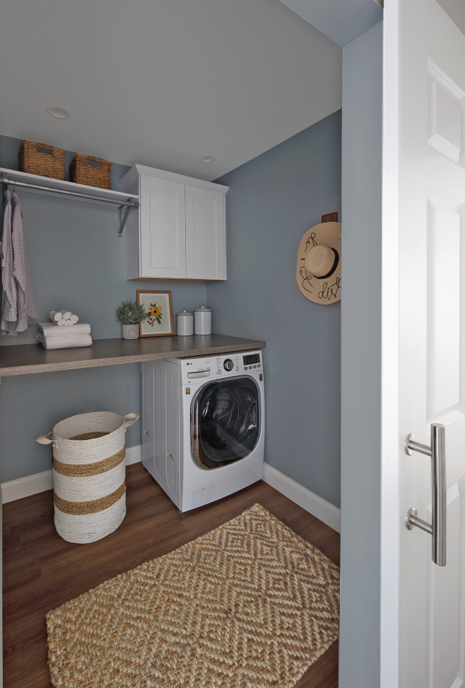 Small traditional galley laundry cupboard in Philadelphia with a belfast sink, shaker cabinets, white cabinets, laminate countertops, white splashback, ceramic splashback, blue walls, vinyl flooring, an integrated washer and dryer, brown floors and grey worktops.