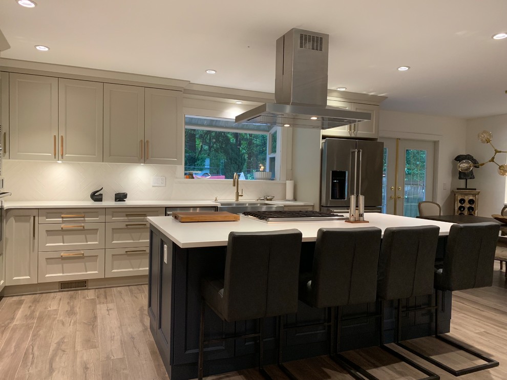 This is an example of a large arts and crafts l-shaped open plan kitchen in Vancouver with a farmhouse sink, shaker cabinets, beige cabinets, quartz benchtops, white splashback, ceramic splashback, stainless steel appliances, laminate floors, with island, grey floor and white benchtop.