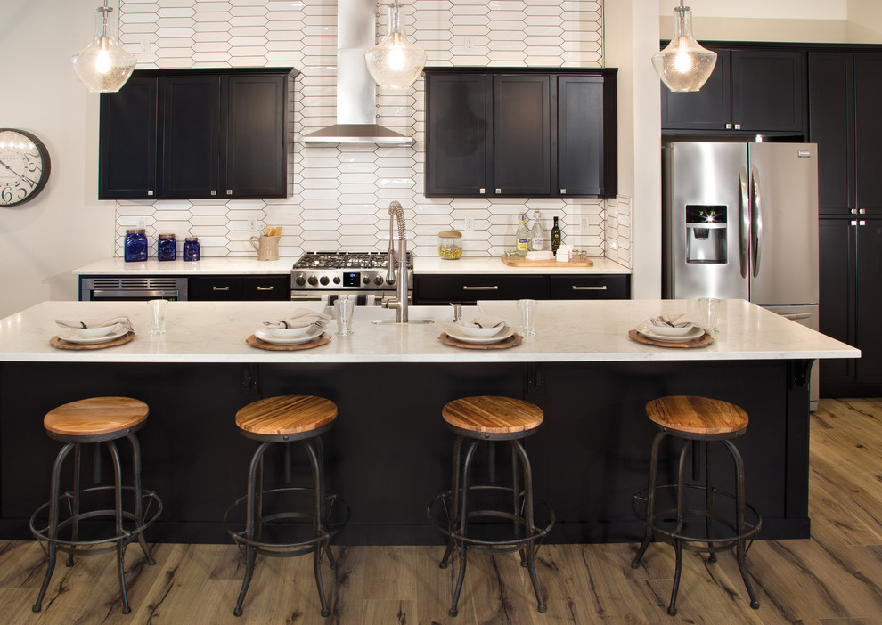 Minimalist kitchen photo with shaker cabinets, black cabinets, white backsplash, stainless steel appliances and an island