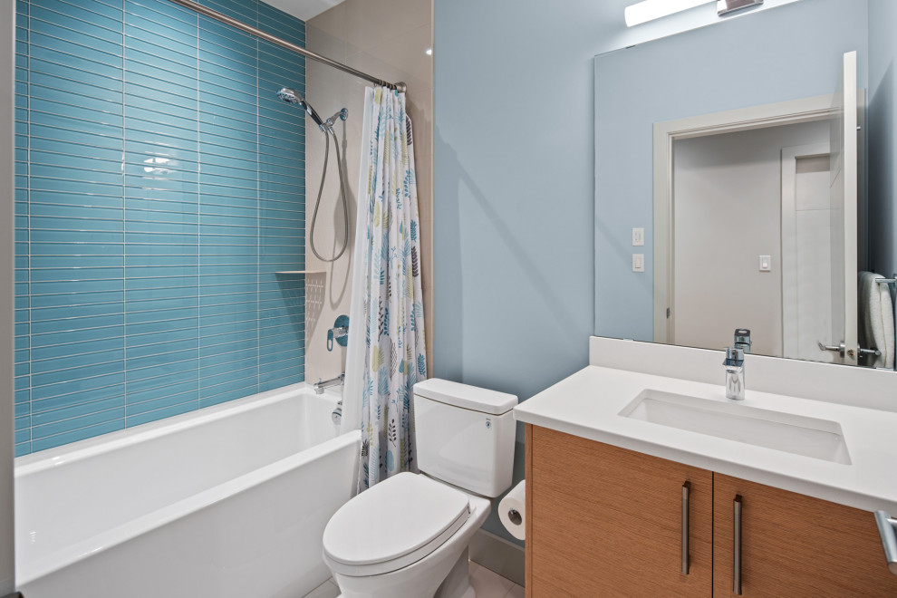 This is an example of a contemporary 3/4 bathroom in Vancouver with flat-panel cabinets, brown cabinets, an alcove tub, a shower/bathtub combo, a two-piece toilet, blue tile, glass tile, blue walls, porcelain floors, an undermount sink, engineered quartz benchtops, grey floor, a shower curtain, white benchtops, a single vanity and a floating vanity.
