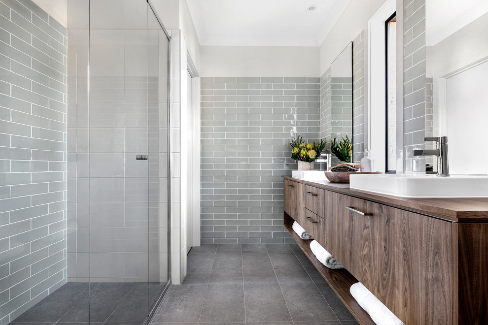 Inspiration for a beach style bathroom in Other with flat-panel cabinets, dark wood cabinets, a curbless shower, gray tile, white tile, white walls, a drop-in sink, wood benchtops, grey floor and brown benchtops.