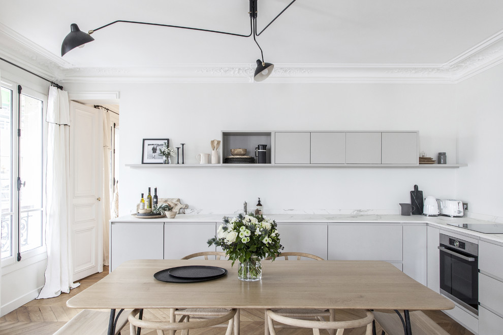 Photo of a mid-sized scandinavian l-shaped eat-in kitchen in Paris with grey cabinets, white splashback, black appliances, no island, white benchtop, flat-panel cabinets, marble benchtops, marble splashback, medium hardwood floors and brown floor.