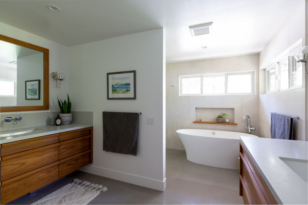 Large transitional master gray tile and ceramic tile ceramic tile and gray floor freestanding bathtub photo with furniture-like cabinets, brown cabinets, a two-piece toilet, white walls, a drop-in sink, quartz countertops and gray countertops