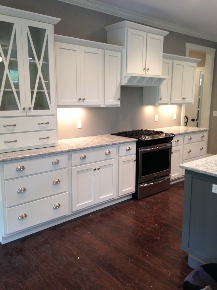 Small transitional single-wall medium tone wood floor and brown floor eat-in kitchen photo with glass-front cabinets, white cabinets, granite countertops, black appliances and an island