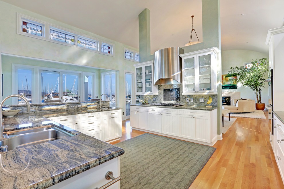Large beach style l-shaped open plan kitchen in San Francisco with an undermount sink, glass-front cabinets, white cabinets, stainless steel appliances and medium hardwood floors.