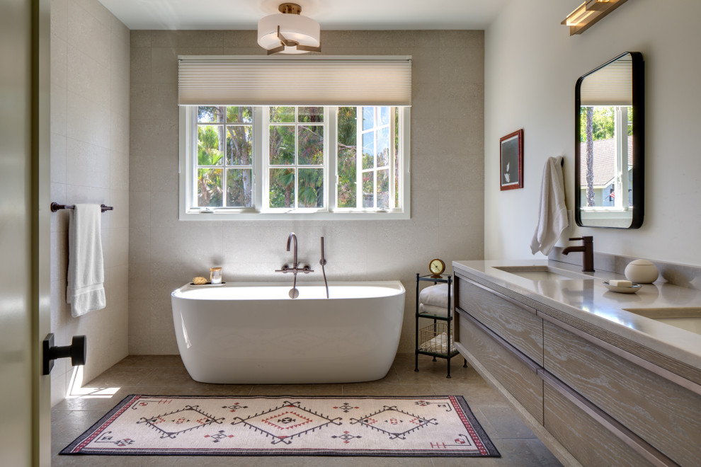 This is an example of a large eclectic master bathroom in San Diego with flat-panel cabinets, grey cabinets, a freestanding tub, an alcove shower, a one-piece toilet, white tile, porcelain tile, white walls, limestone floors, an undermount sink, solid surface benchtops, grey floor, a hinged shower door, grey benchtops, a shower seat, a double vanity and a floating vanity.