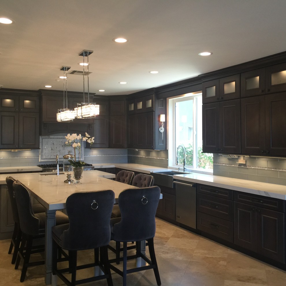 Inspiration for a mid-sized transitional l-shaped travertine floor and beige floor enclosed kitchen remodel in Orange County with a farmhouse sink, beaded inset cabinets, brown cabinets, marble countertops, gray backsplash, glass tile backsplash, stainless steel appliances and an island