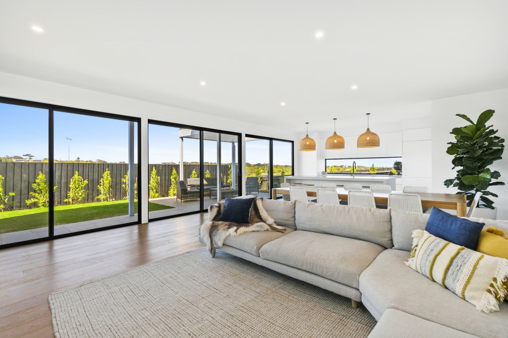 Design ideas for a mid-sized contemporary open concept living room in Geelong with white walls, light hardwood floors, a standard fireplace, a plaster fireplace surround and a freestanding tv.
