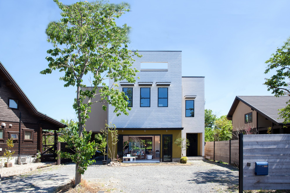 Photo of a large contemporary three-storey brick white house exterior in Kyoto with a shed roof and a metal roof.