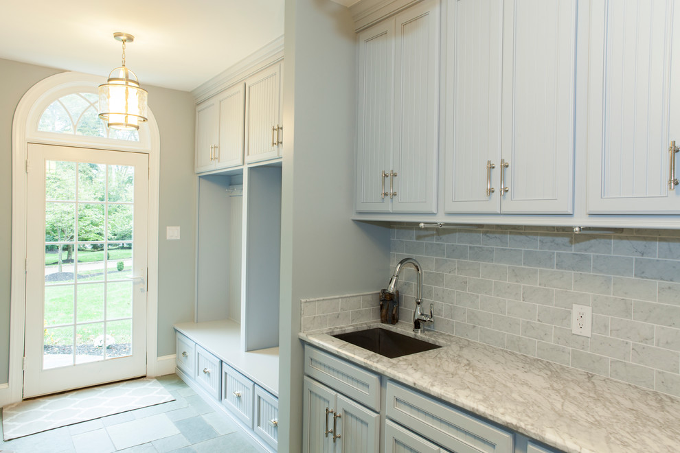 Inspiration for a large traditional single-wall utility room in Philadelphia with an undermount sink, recessed-panel cabinets, grey cabinets, marble benchtops, grey walls, ceramic floors and a stacked washer and dryer.