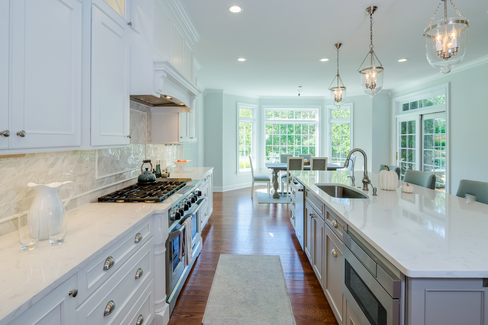 Inspiration for a large transitional l-shaped eat-in kitchen in Philadelphia with an undermount sink, flat-panel cabinets, white cabinets, quartz benchtops, white splashback, porcelain splashback, stainless steel appliances, medium hardwood floors, with island and brown floor.