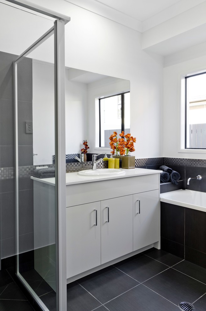 Photo of a mid-sized contemporary kids bathroom in Brisbane with a drop-in sink, flat-panel cabinets, white cabinets, engineered quartz benchtops, a drop-in tub, a corner shower, black tile, ceramic tile, white walls and ceramic floors.